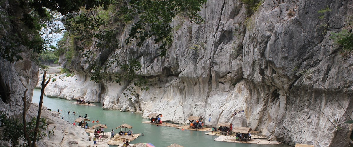 A river with people on boats and platforms, surrounded by rocky cliffs.