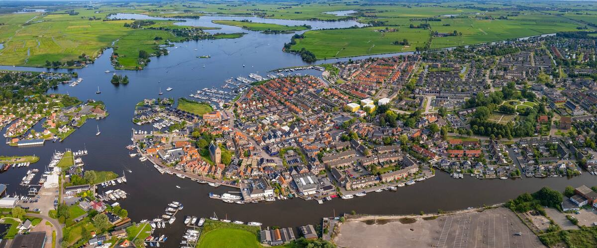 An aerial view of a town with a river, boats, and surrounding fields.