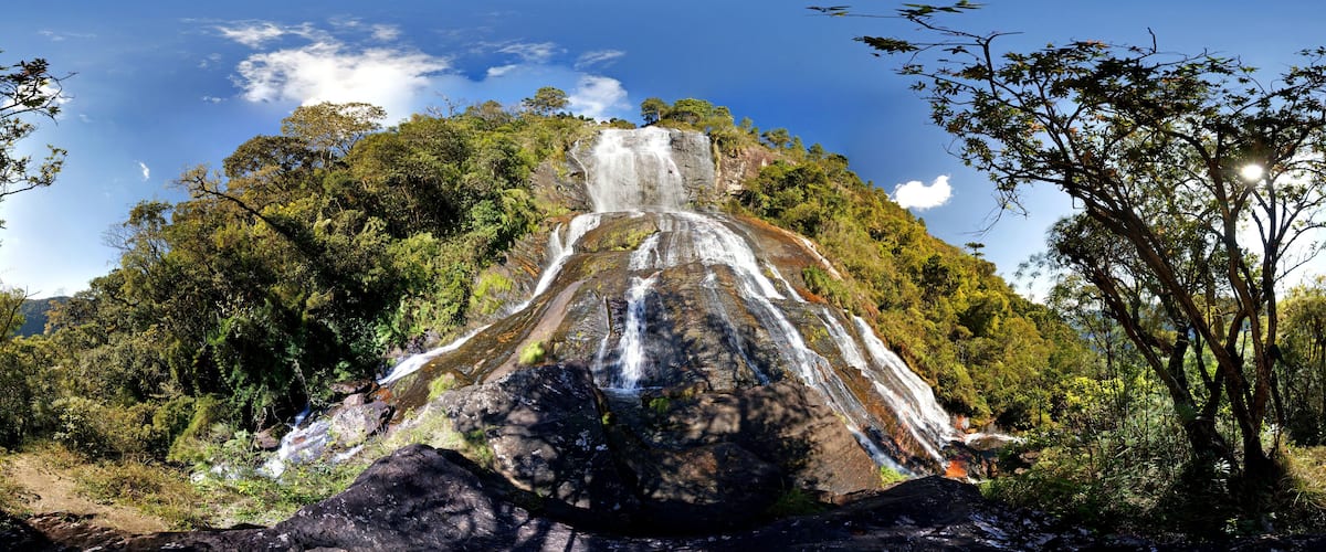 A waterfall cascading down a rocky hill surrounded by dense green foliage.