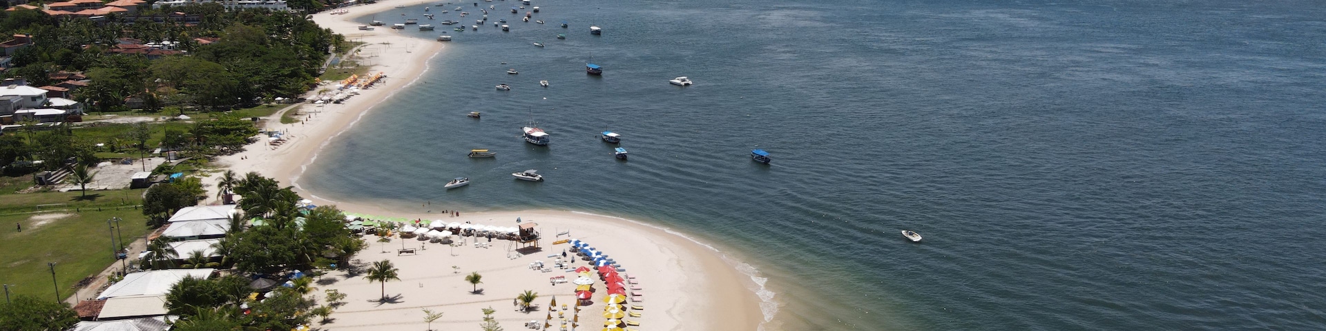 Vista aérea de una zona costera con playa, barcos y un pueblo al fondo.