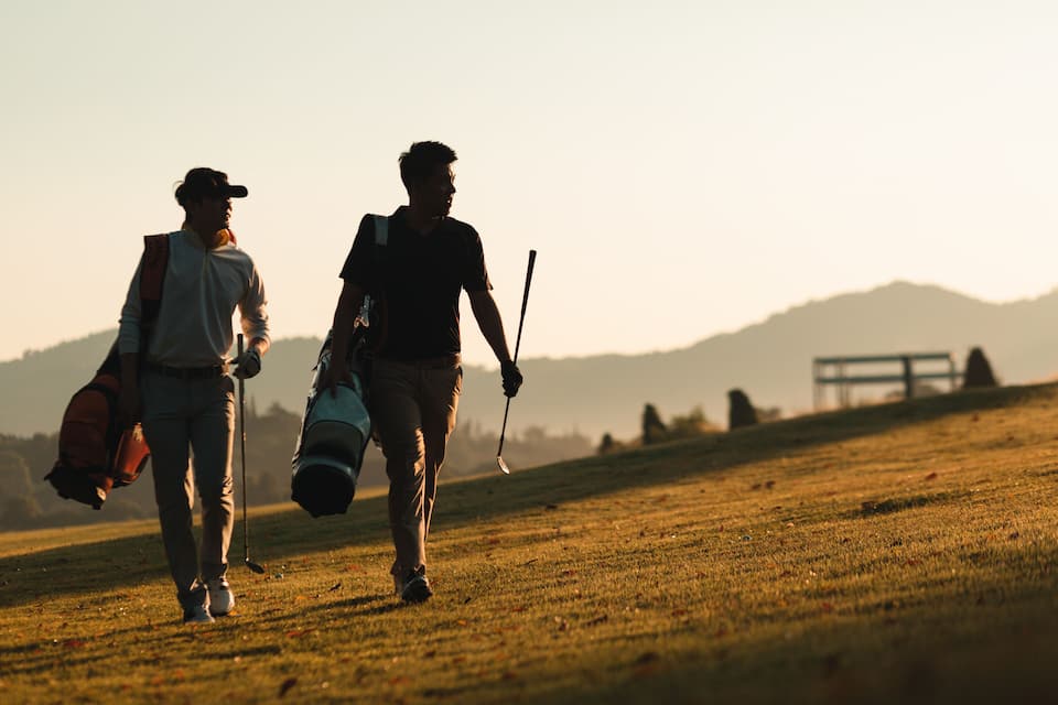 Two people walking on a grassy hill with a mountain in the background.