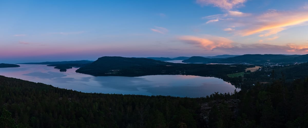 A lake surrounded by forested hills during twilight.
