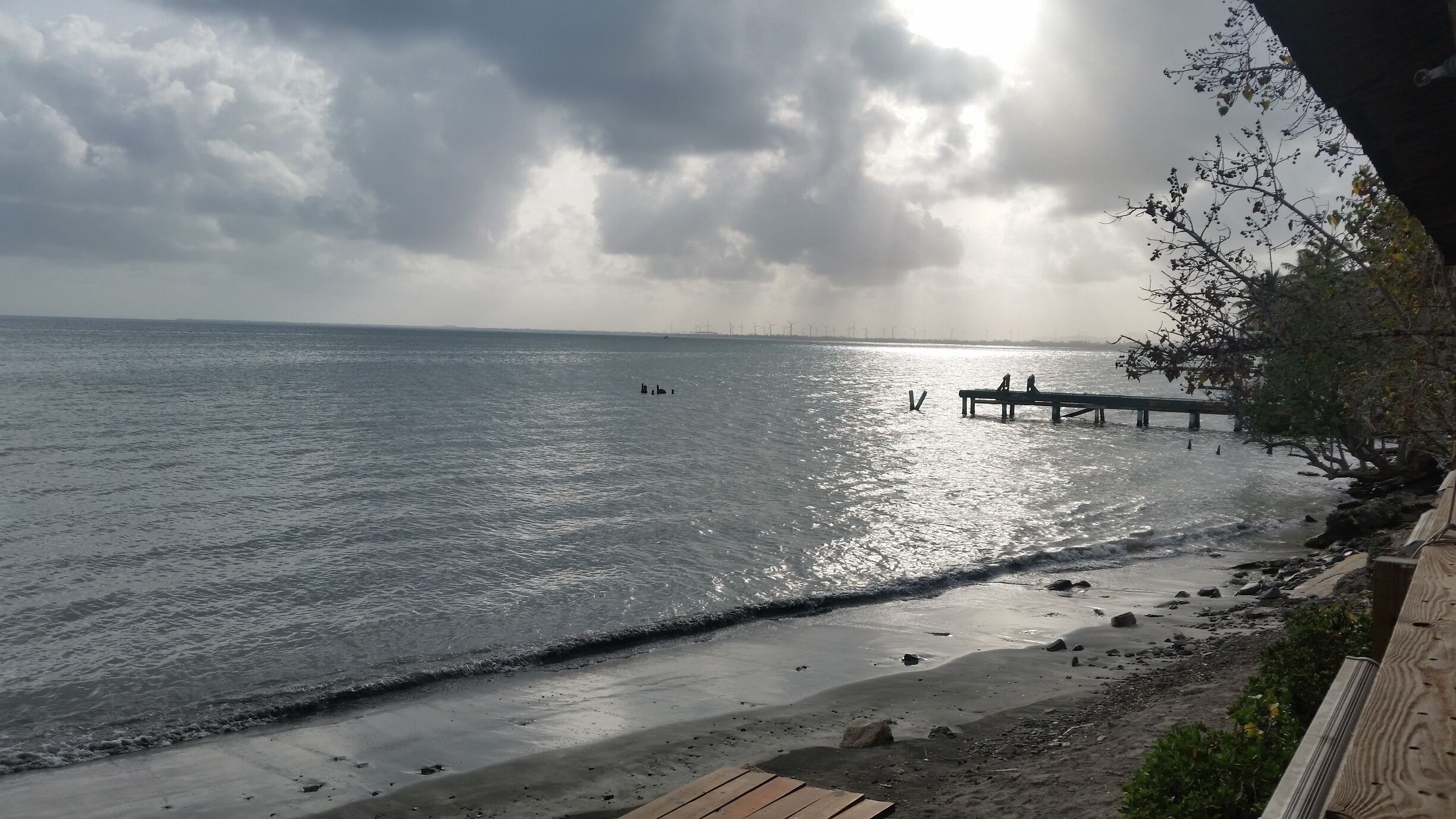A beach with a wooden pier extending into the water, a rocky shoreline, and a cloudy sky.
