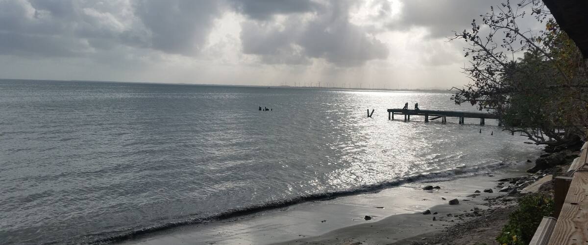 A beach with a wooden pier extending into the water, a rocky shoreline, and a cloudy sky.