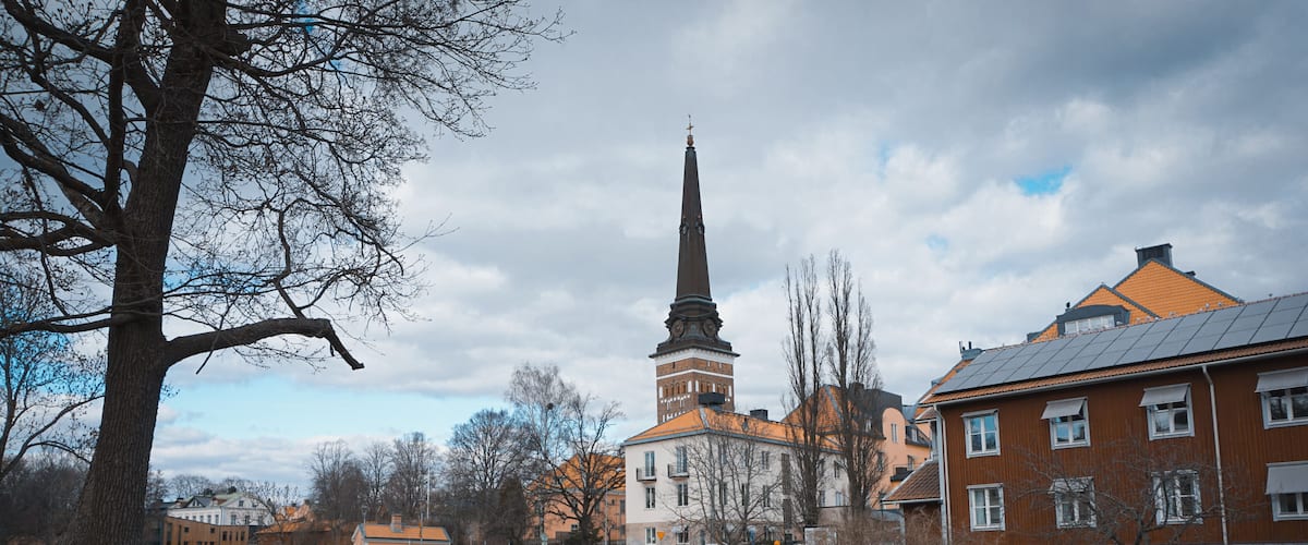 A river with a stone wall, a bridge, a church with a tall spire, and residential buildings.