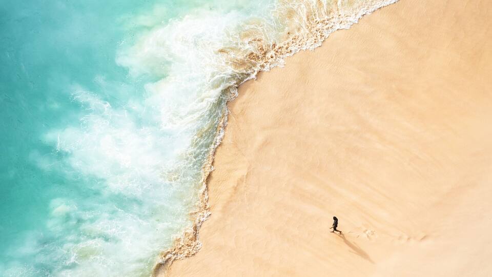 A sandy beach with ocean waves and a single person walking.