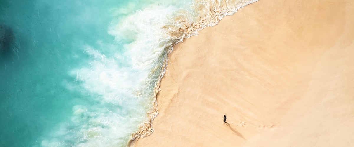 A sandy beach with ocean waves and a single person walking.
