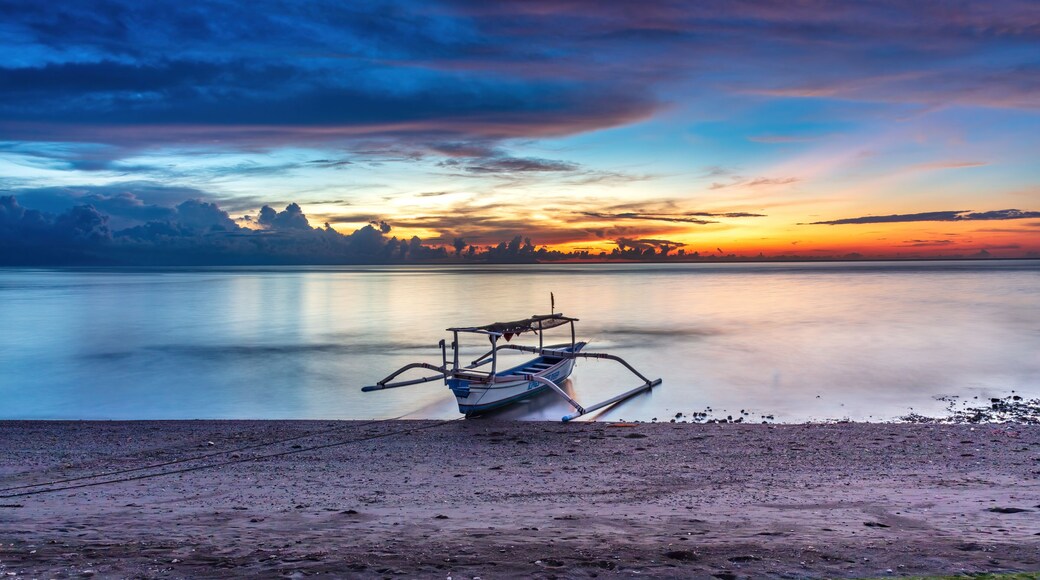 Ocean sunset at Lovina Beach, northern Bali, Indonesia. Beach with boat in theforeground; setting sun surrounded by colorful clouds. Sun's reflection on the water.