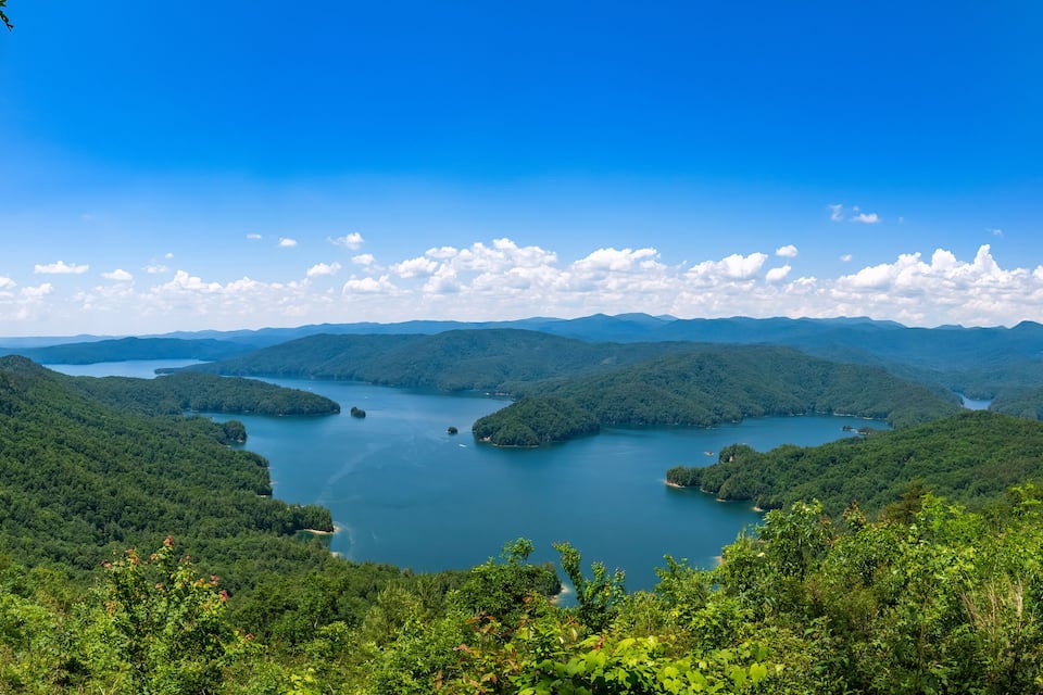A lake surrounded by forested hills under a clear blue sky.