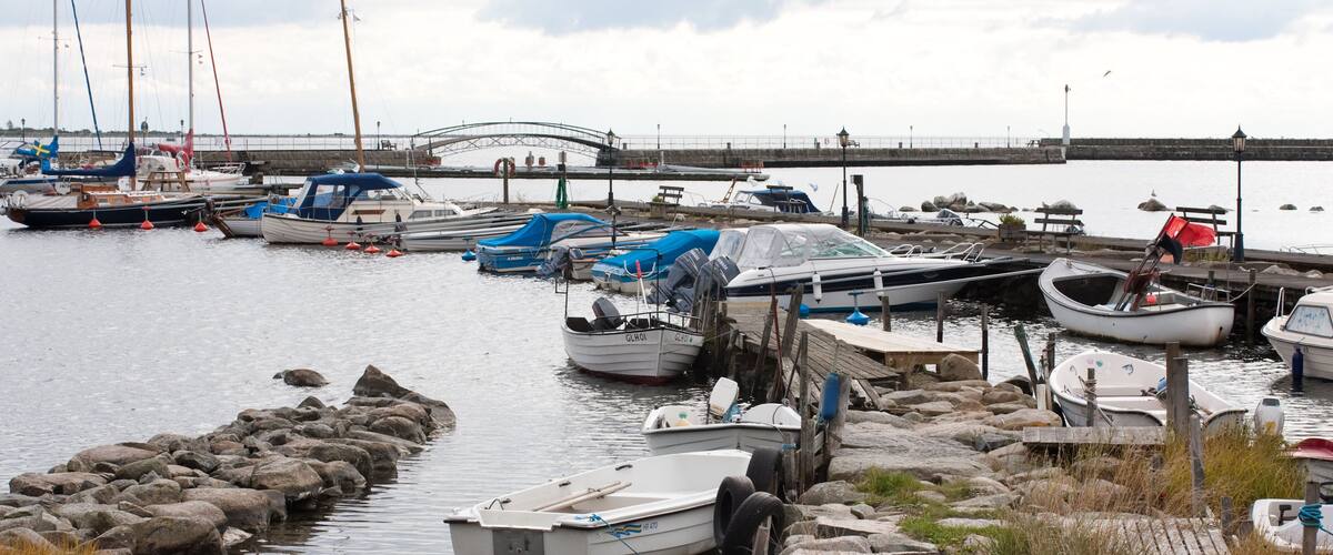 A marina with various boats docked, a rocky shoreline, and a bridge in the background.