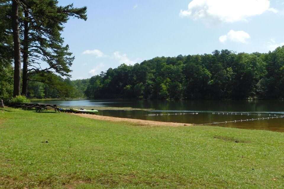 A grassy lakeside area with picnic tables and kayaks.