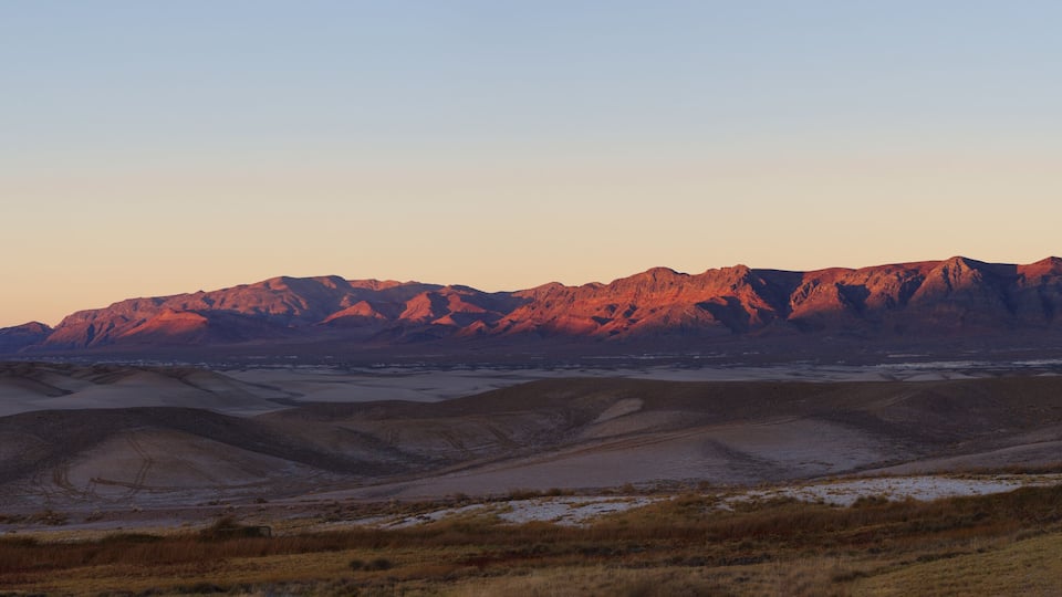 A desert landscape with sand dunes and a mountain range in the background.