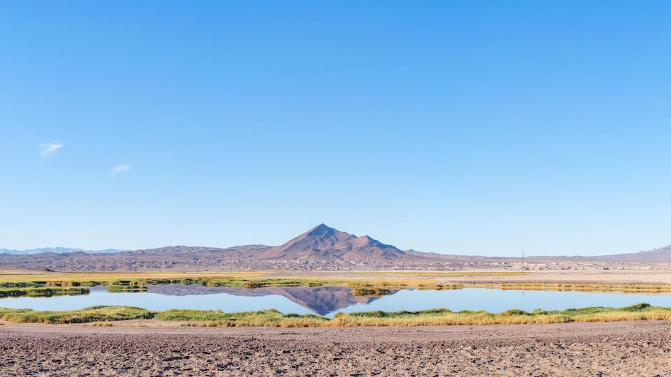 A desert landscape with a mountain range, a small lake, and sparse vegetation.