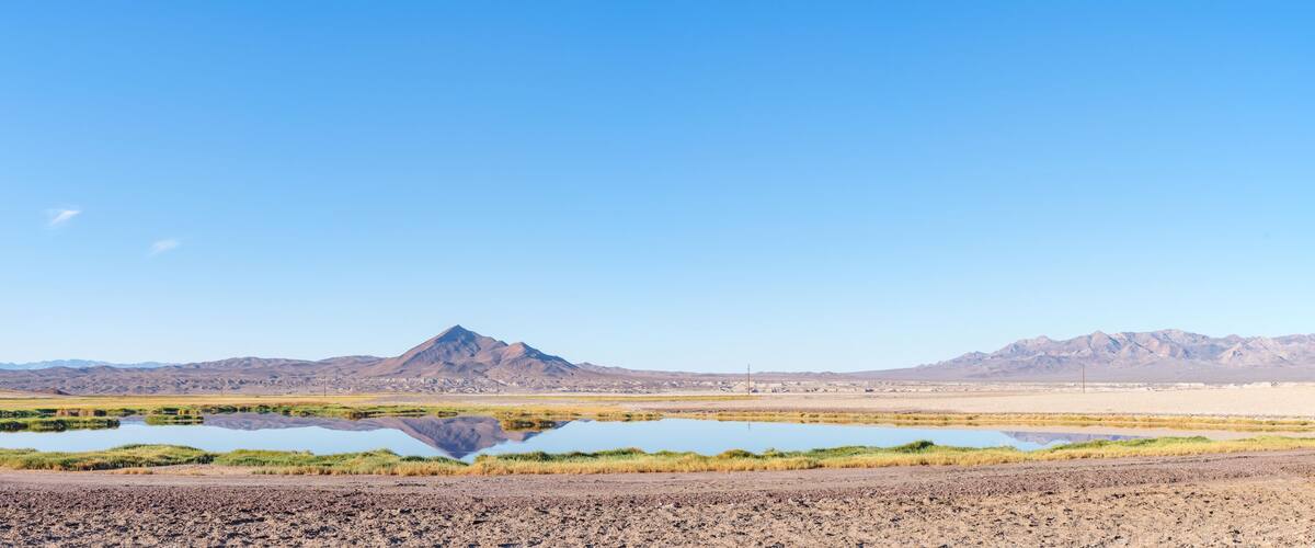 A desert landscape with a mountain range, a small lake, and sparse vegetation.