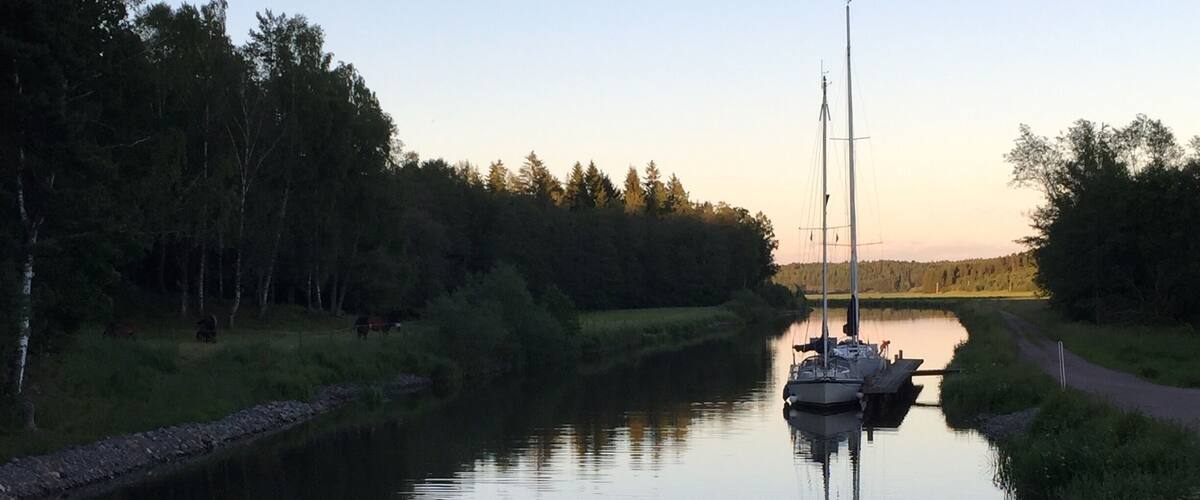 A calm river with a wooden dock and a sailboat anchored in the distance.