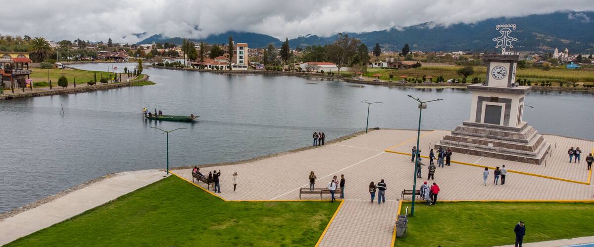Ein Flussuferpark mit einem Denkmal, einem Boot auf dem Wasser und einer Bergkulisse im Hintergrund.