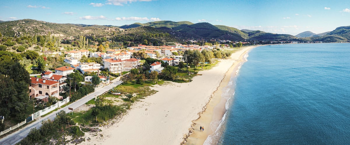 A coastal town with a beach, houses, and mountains in the background.