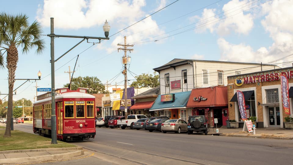 A trolley on a street with buildings and parked cars.