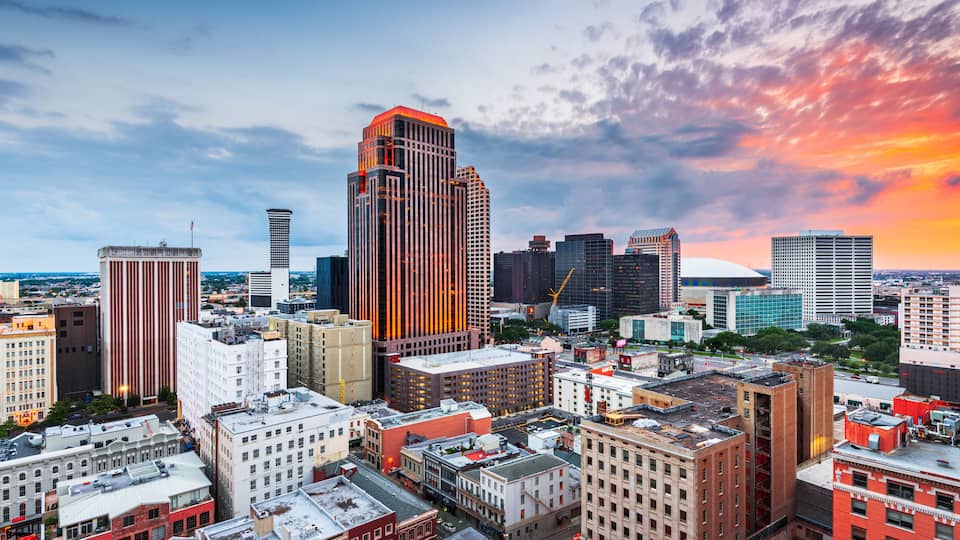 A city skyline with a prominent tall building, various mid-rise buildings, and a sunset sky.