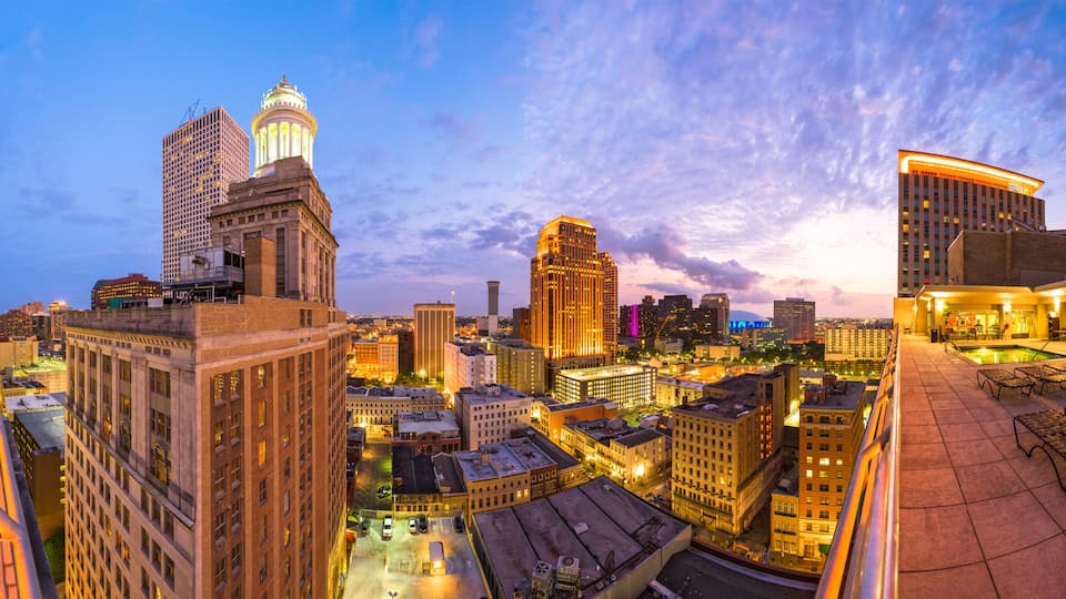 A cityscape at dusk with illuminated buildings, a prominent dome structure, and a modern hotel with a rooftop pool.