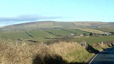 A rural road winding through rolling hills with fields and scattered houses.