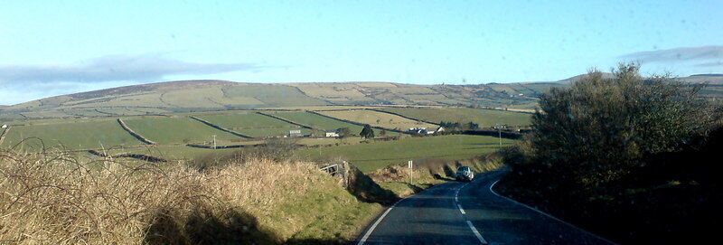 A rural road winding through rolling hills with fields and scattered houses.