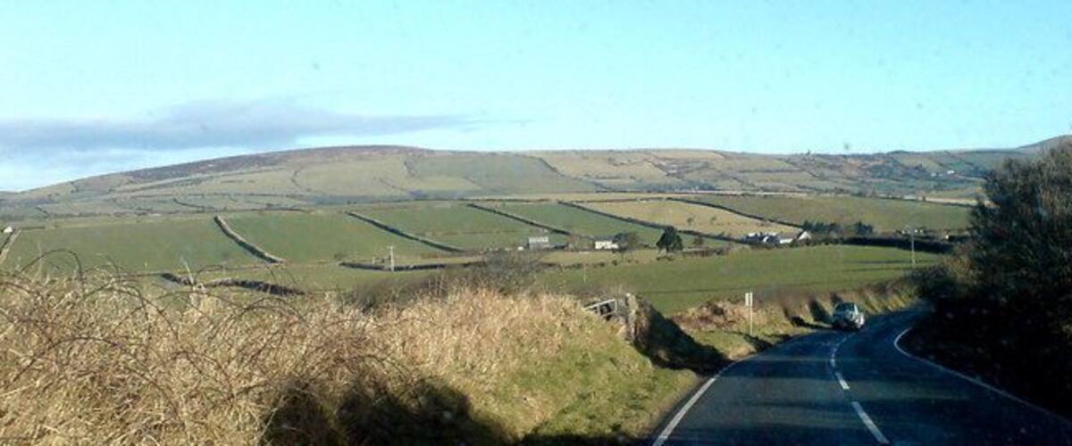 A rural road winding through rolling hills with fields and scattered houses.