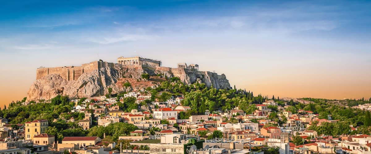 A historic cityscape with a prominent ancient fortress on a hill, surrounded by dense greenery and residential buildings.