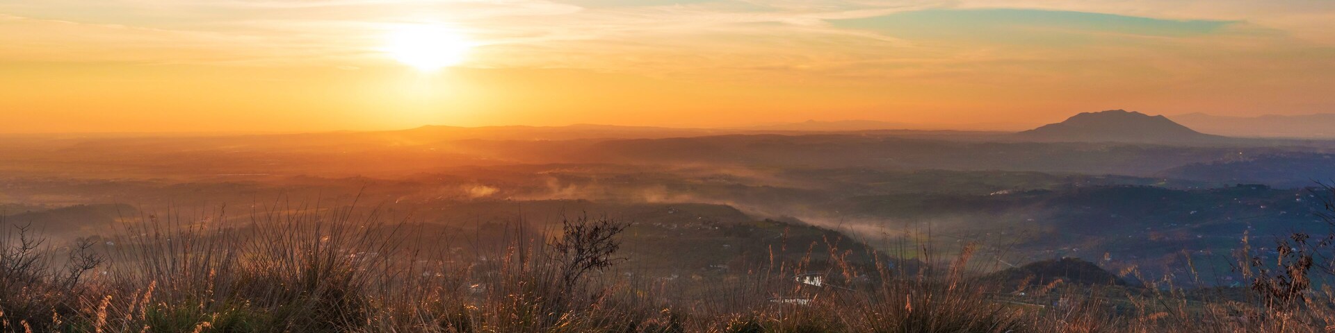 Amanecer sobre un paisaje montañoso con cielo despejado y colinas distantes.