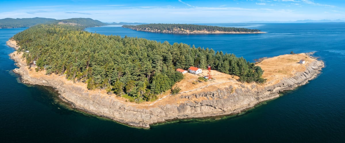 An aerial view of a forested island with a small settlement and a lighthouse.