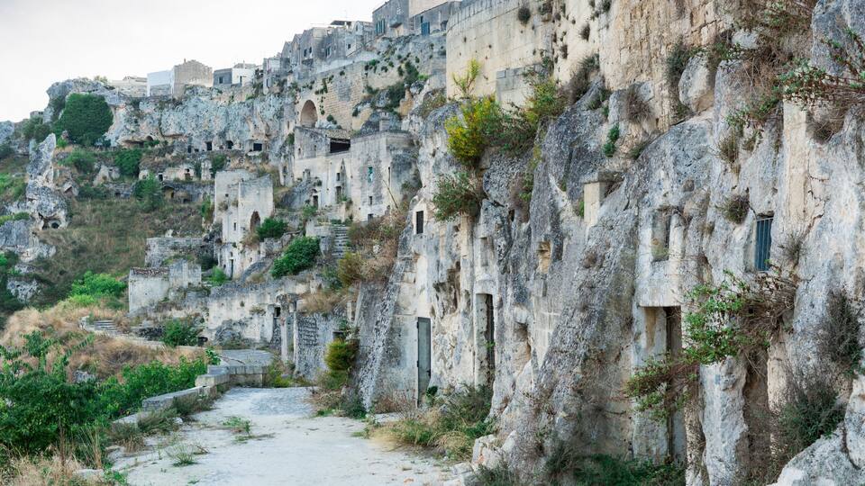 A rugged mountain path with ancient stone buildings and greenery.