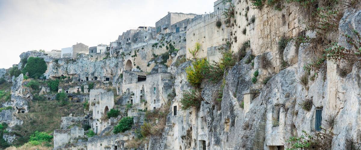 A rugged mountain path with ancient stone buildings and greenery.