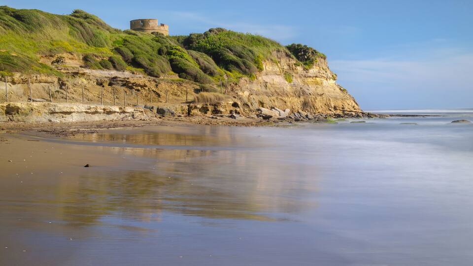 A coastal landscape with a grassy cliff and a circular stone structure.