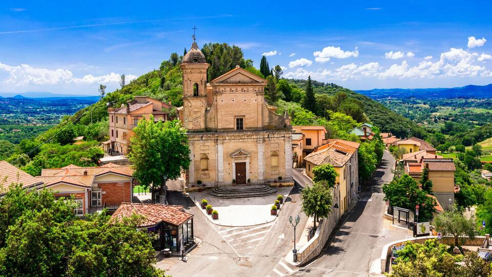 A historic church on a hilltop surrounded by lush greenery and a valley.