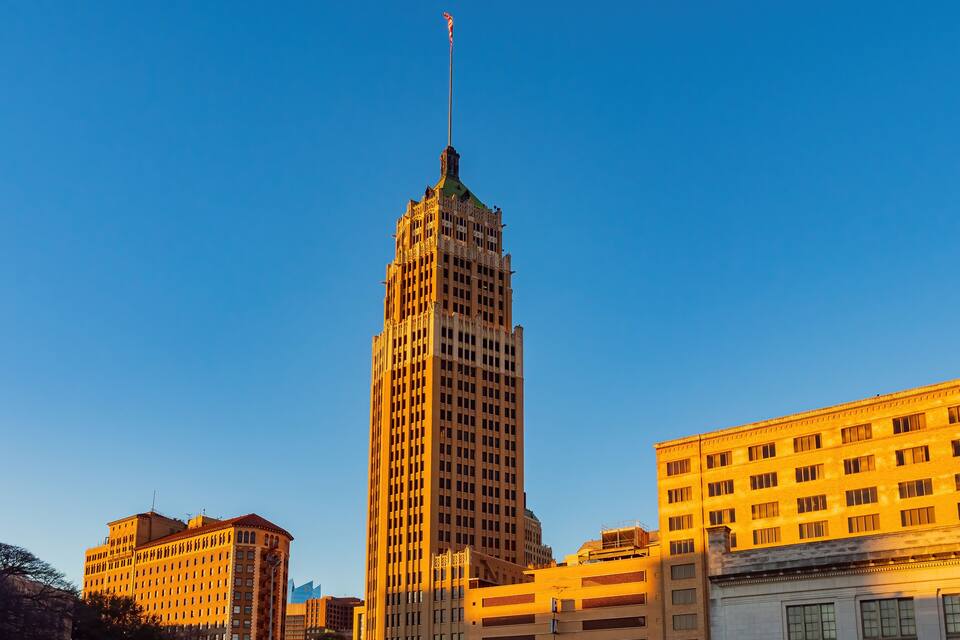 A tall building with a flag on top, surrounded by other buildings.