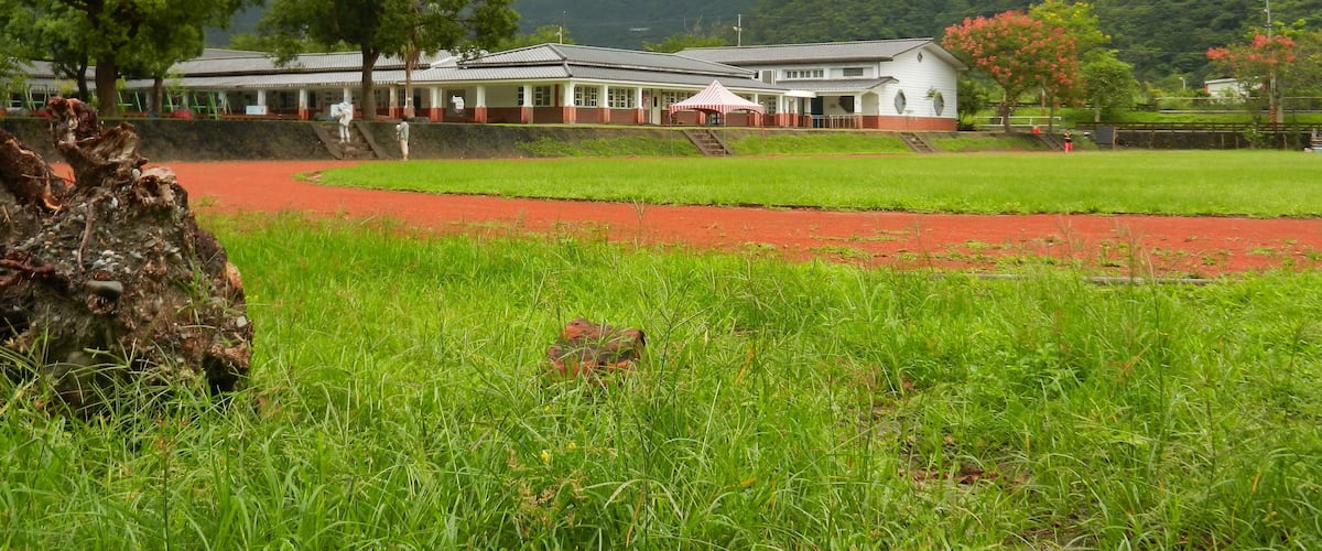 A traditional building with a red and white facade, surrounded by lush green fields and a mountainous backdrop.