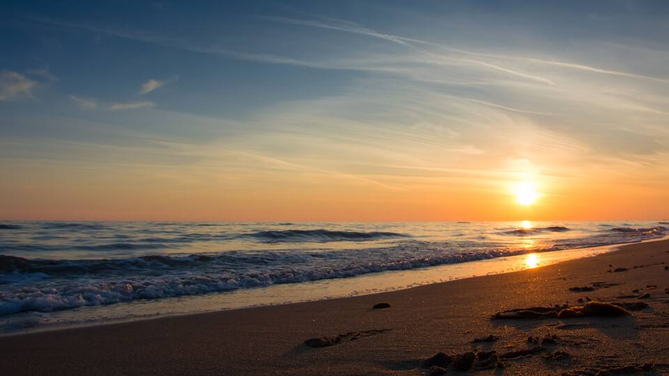 A sunset over a beach with footprints in the sand.