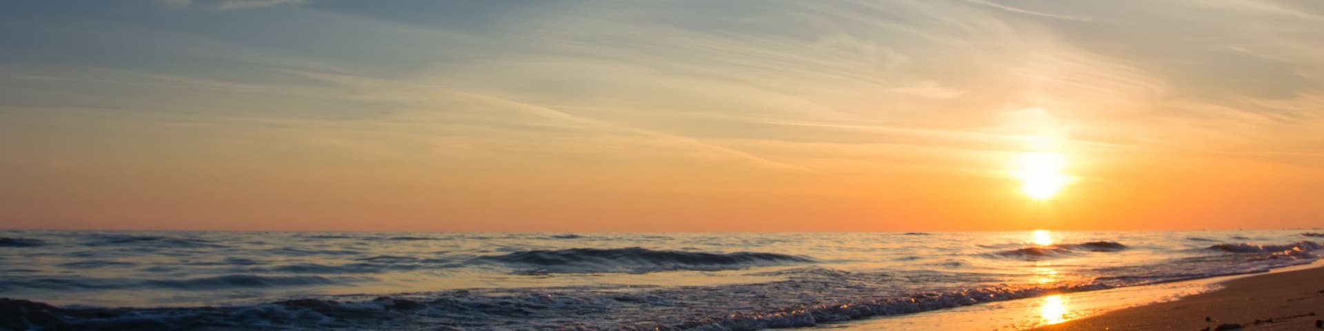 Una puesta de sol sobre una playa con huellas en la arena.