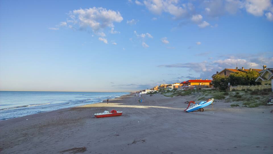 A beach with a red and blue boat, houses, and a clear sky.