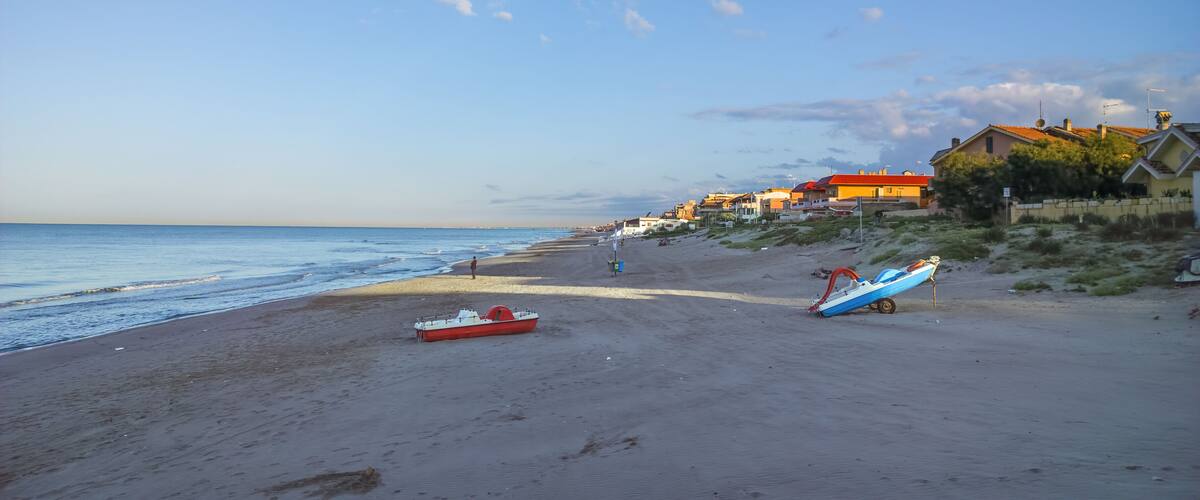 A beach with a red and blue boat, houses, and a clear sky.