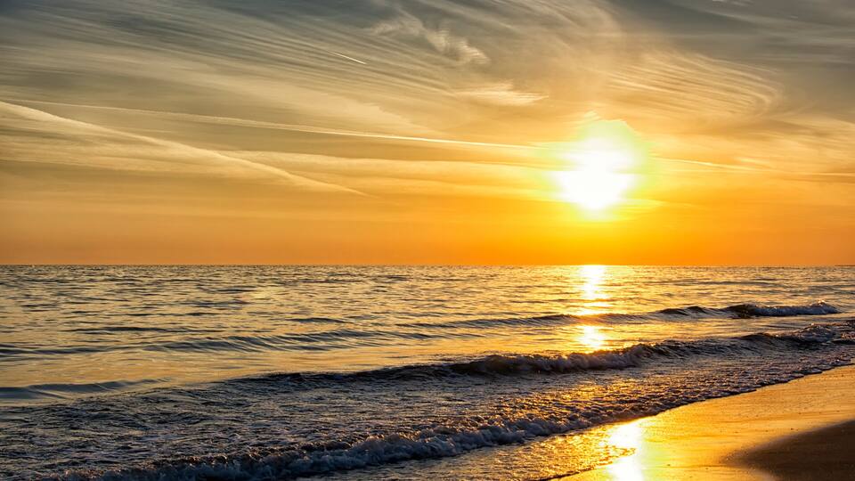 A sunset over the ocean with waves on the shore.
