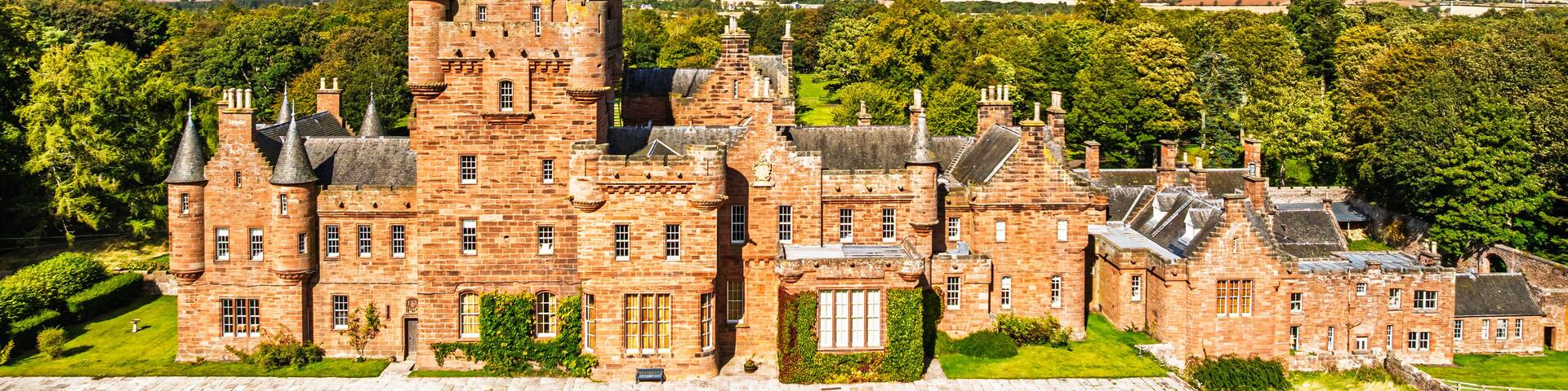 A large, historic castle with multiple towers and turrets, surrounded by lush greenery and a clear blue sky.