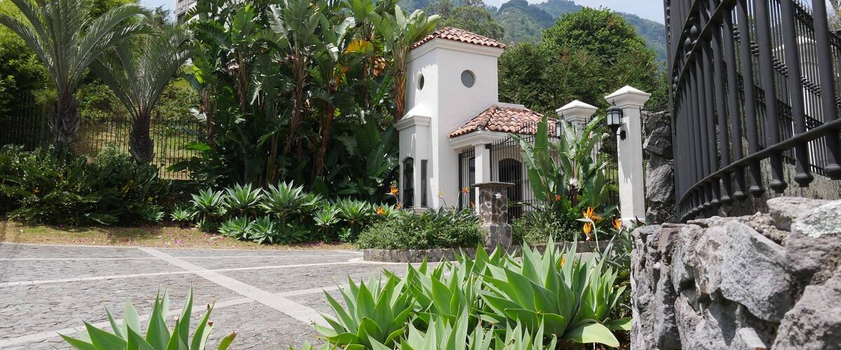 A white church with a bell tower, surrounded by lush greenery and a stone wall.