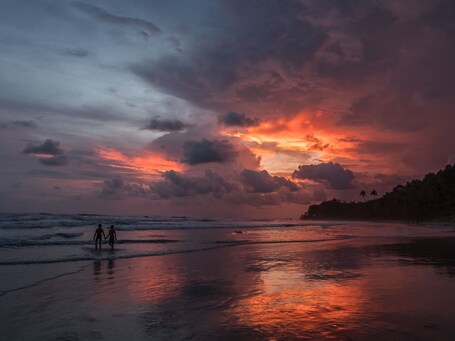 Ein Strand mit Spaziergängern, Wellen und einem Sonnenuntergangshimmel.