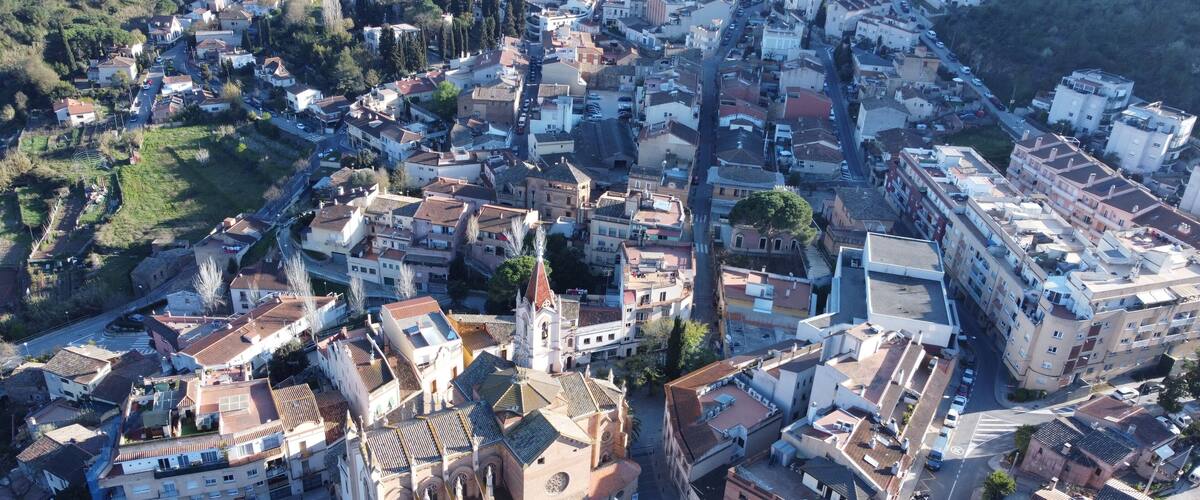 An aerial view of a densely built urban area with a mix of residential and commercial buildings, a prominent church with a bell tower, and a curved road intersection.