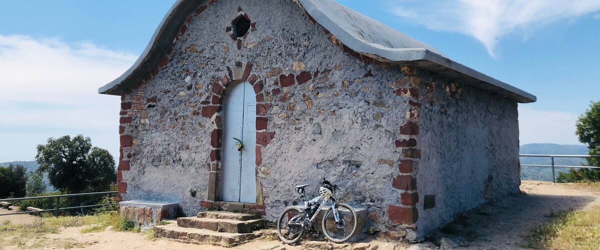 Una pequeña iglesia desgastada por el tiempo con una cruz en la parte superior, una bicicleta estacionada al frente y un cielo azul despejado al fondo.