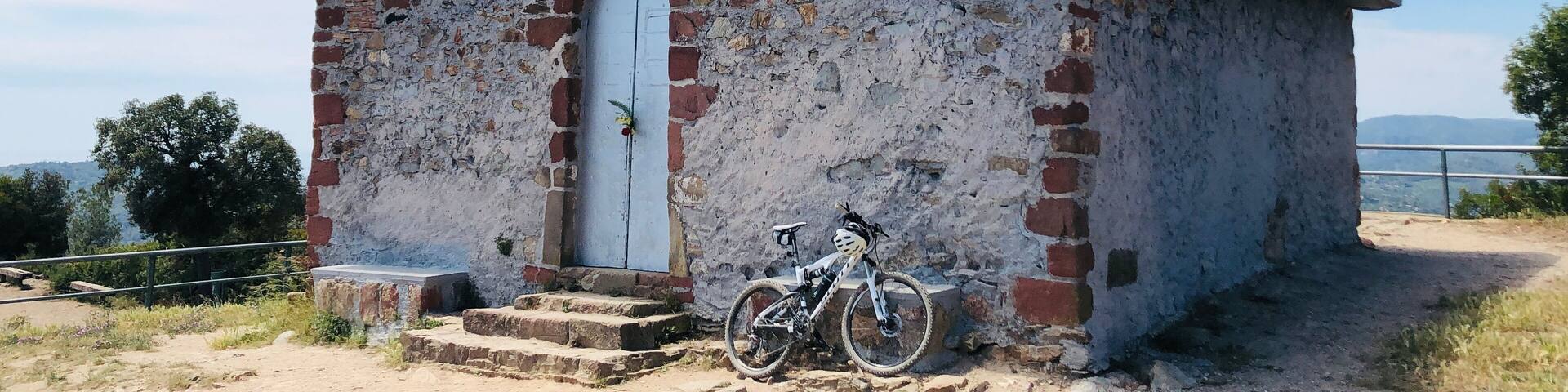 A small, weathered church with a cross on top, a bicycle parked in front, and a clear blue sky in the background.
