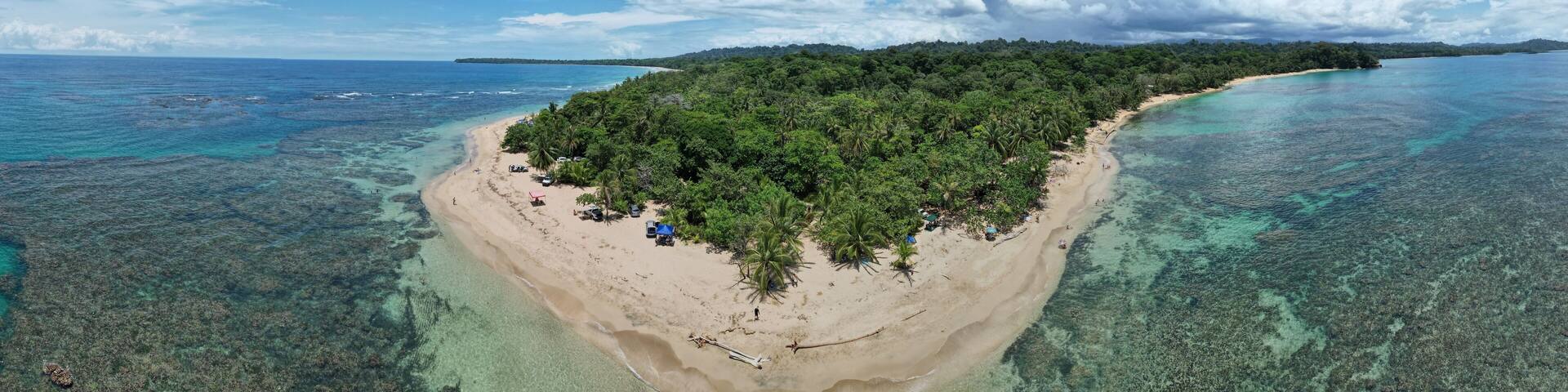 A tropical island with a sandy beach, dense green forest, and clear blue waters.