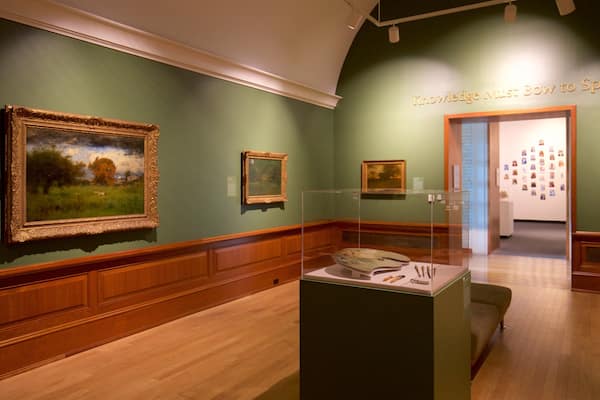 Une galerie d’art où les murs sont ornés de tableaux encadrés et où une vitrine en verre expose des objets d’art.
