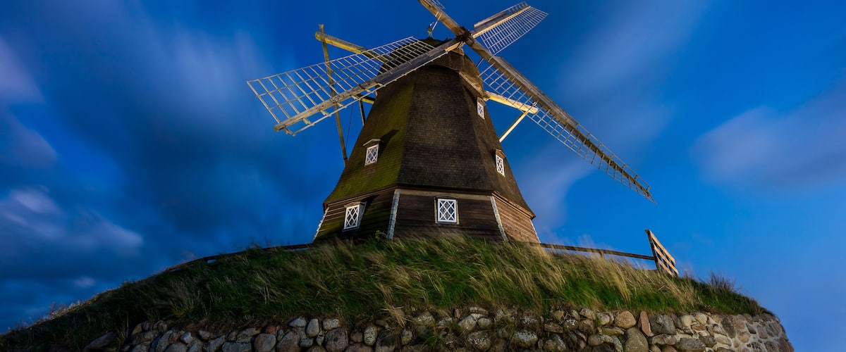 A windmill with a stone base, set against a clear blue sky.